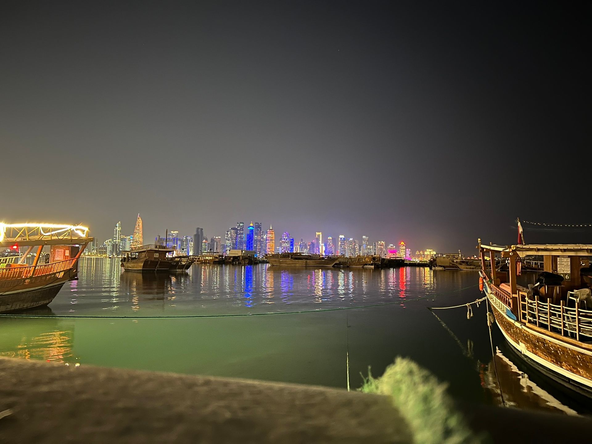 Skyline noturno de Doha com dhows tradicionais atracados na baía